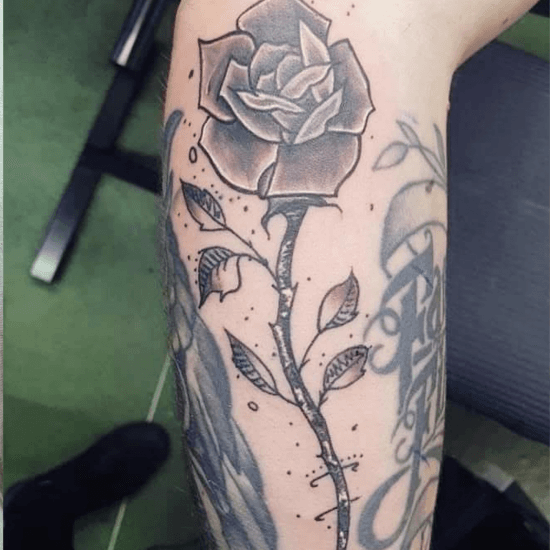 Zwart-wit roos tattoo met steel en bladeren op de onderarm.