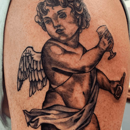 Zwart-wit tattoo van een cherubijn met een bierglas en fles op de bovenarm.