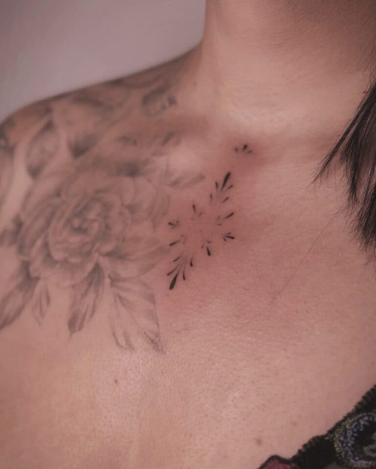 Subtiele, sierlijke ornament tattoo op de borst, naast een oudere bloem.