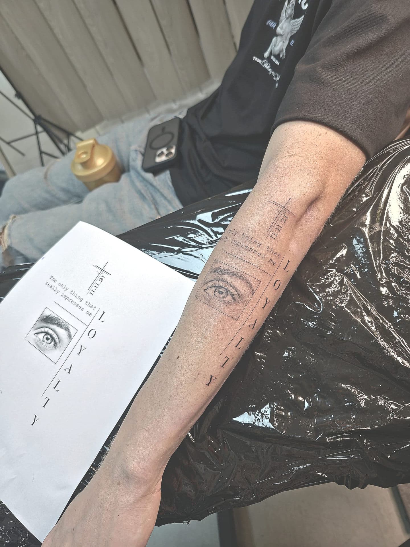 Fineline tattoo op onderarm met oog, tekst en kruis.