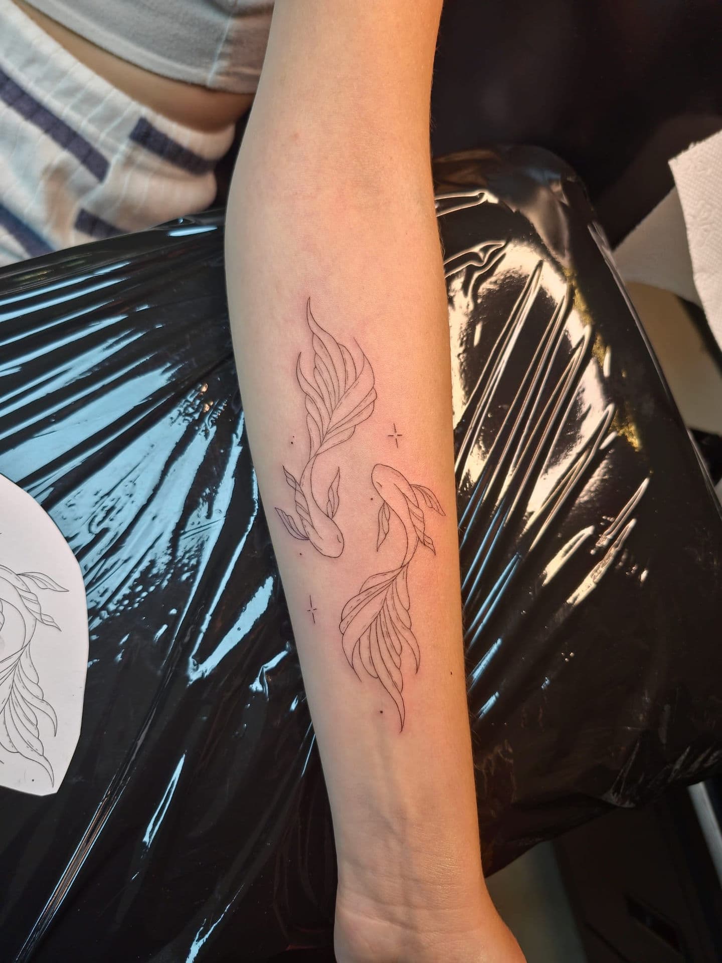 Fineline tattoo van twee vissen die in een cirkel zwemmen op de onderarm.