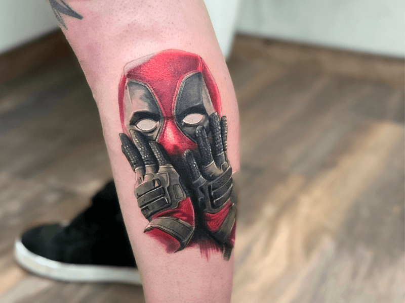 Realistische Deadpool tattoo met handen voor gezicht op onderbeen.