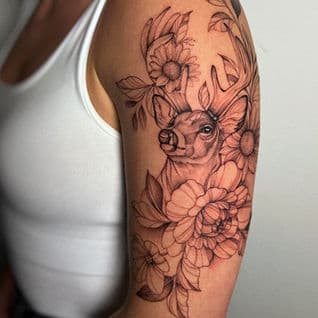 Fineline tattoo van een hert met bloemen op de bovenarm.