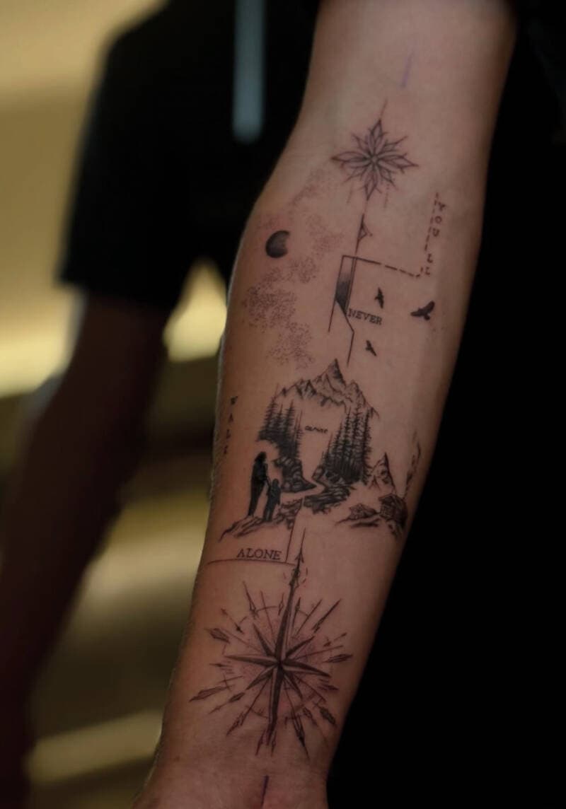 Gedetailleerde fineline tattoo met kompassen, bergen, figuren en tekst op onderarm.
