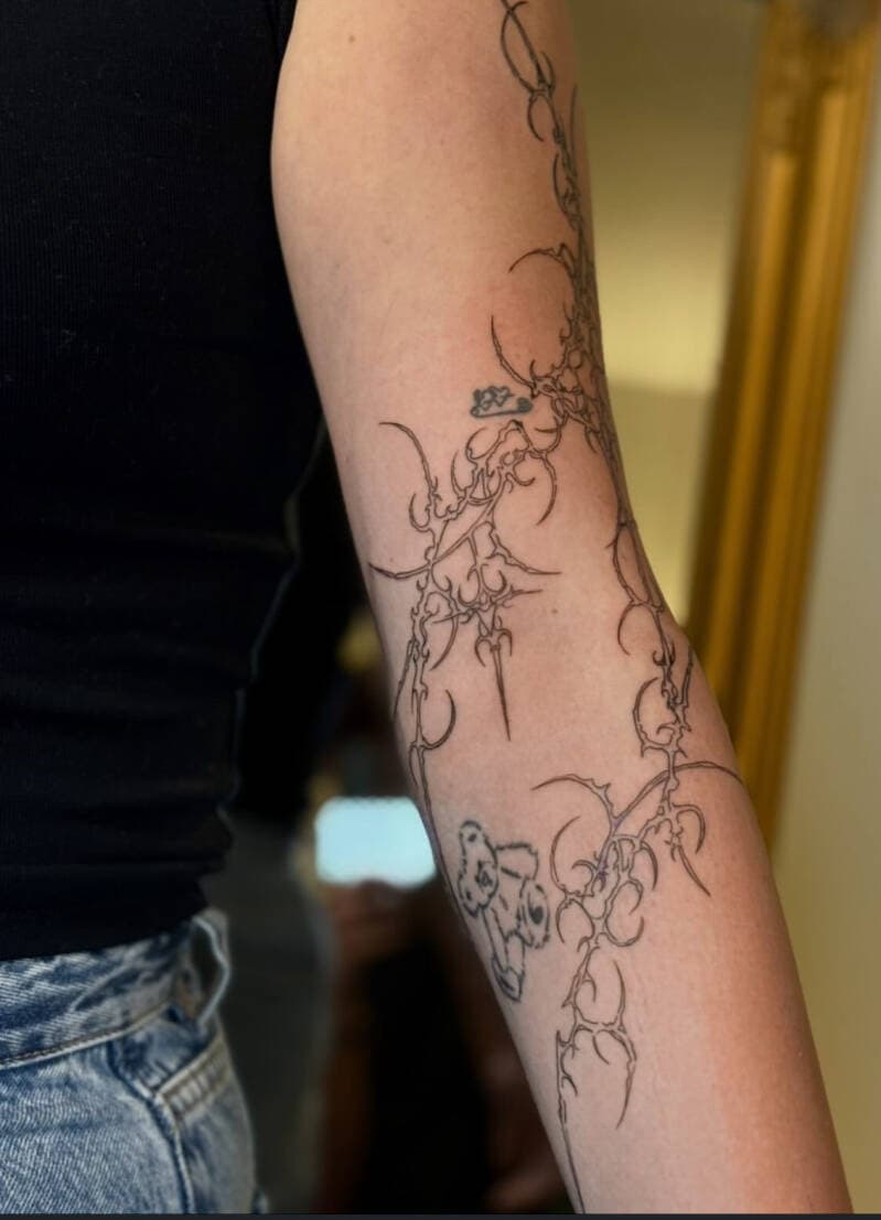 Abstracte fineline tattoo met doornachtige, organische vormen op de arm.