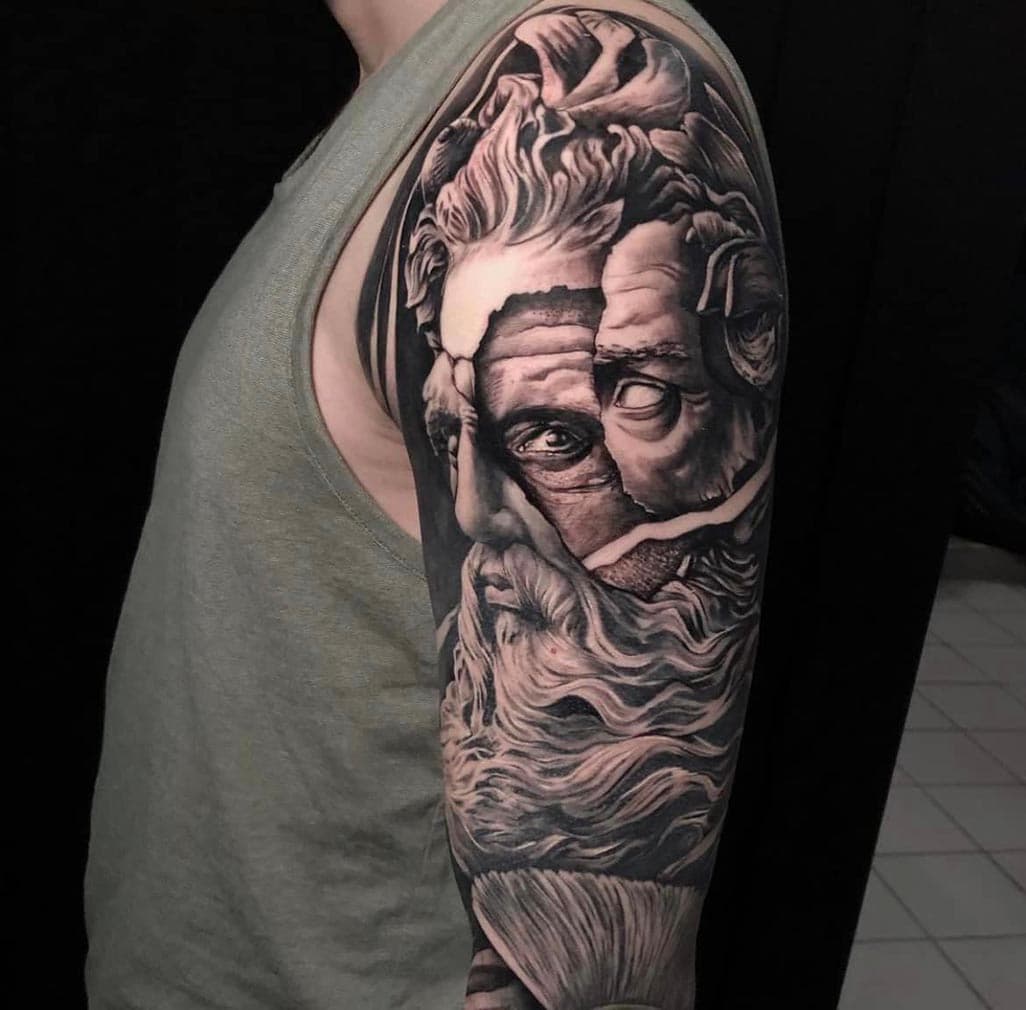 Realistische zwart-wit tattoo van een gebroken Grieks standbeeld op de bovenarm.