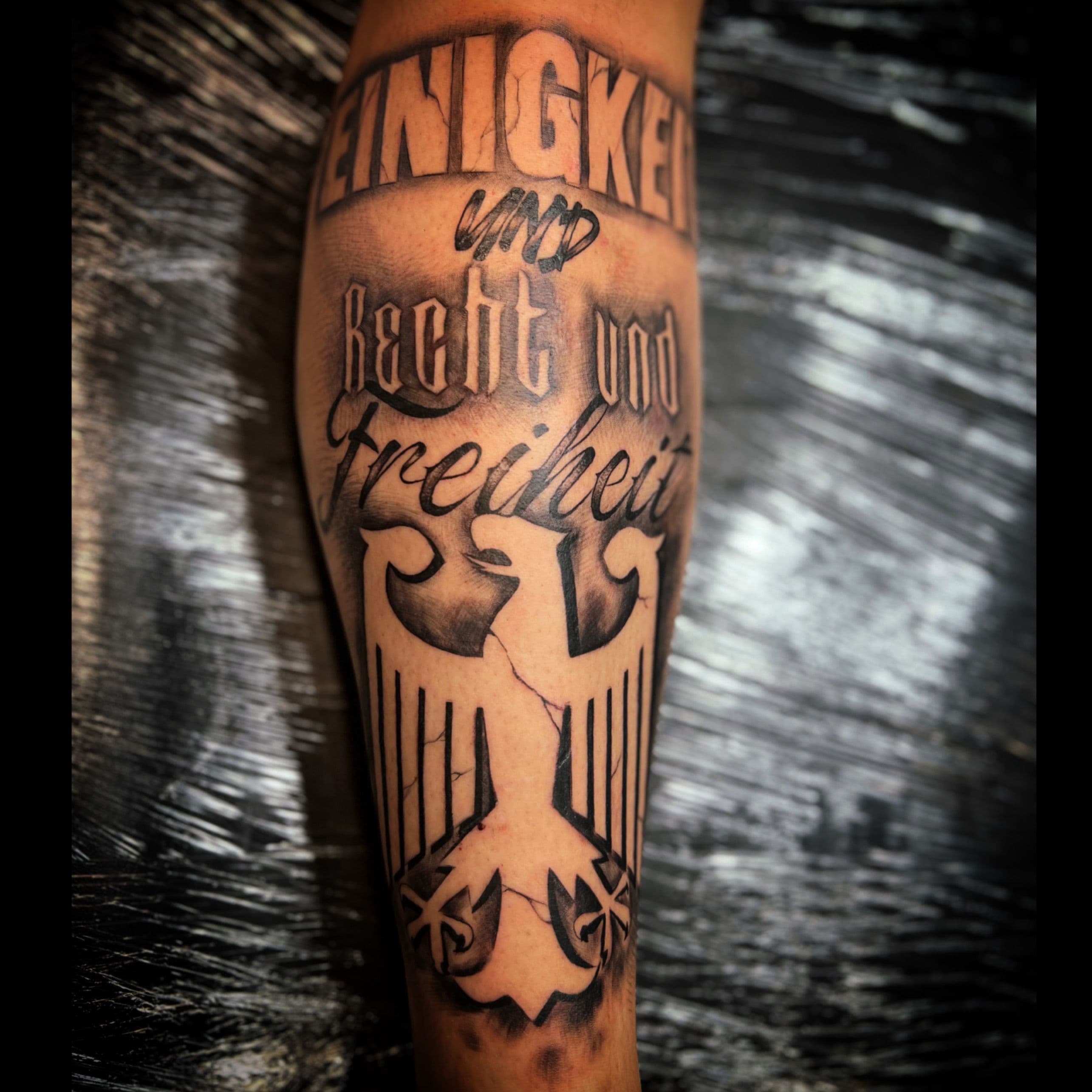 Zwart-wit tattoo van Duitse adelaar en tekst 'Einigkeit und Recht und Freiheit'.