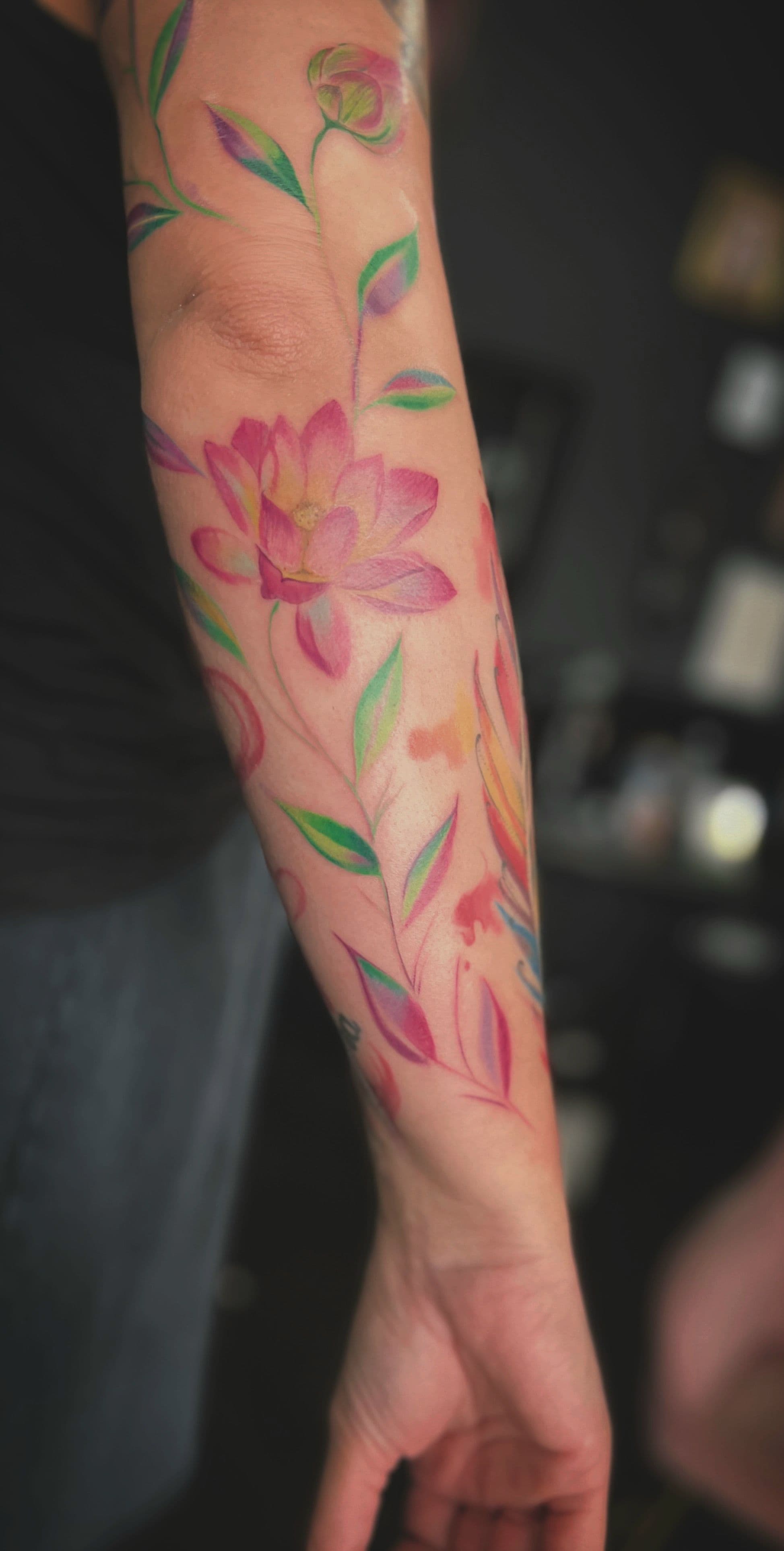 Kleurrijke bloemen en bladeren in aquarel stijl op de onderarm.