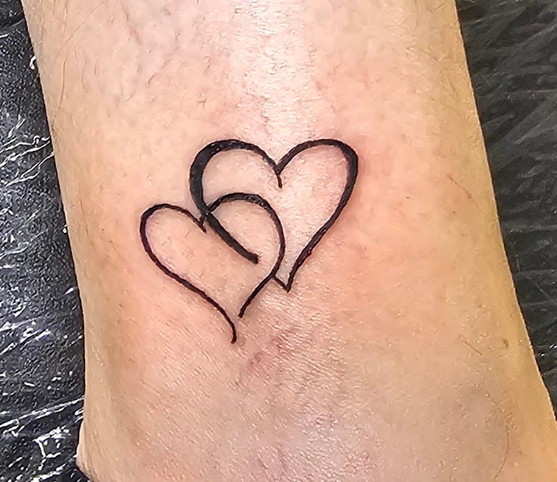 Twee in elkaar verstrengelde harten, minimalistisch lijnwerk op de enkel.