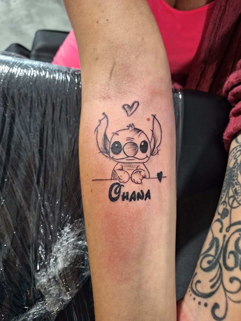 Schattige Stitch tattoo met 'Ohana' tekst en hartjes op de onderarm.