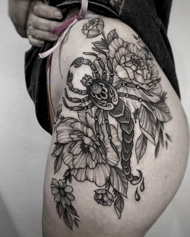 Grote blackwork schorpioen met bloemen op heup en bovenbeen.