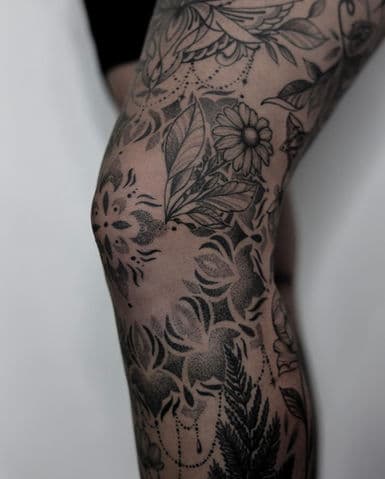 Gedetailleerde blackwork tattoo met bloemen en geometrische patronen op de knie.