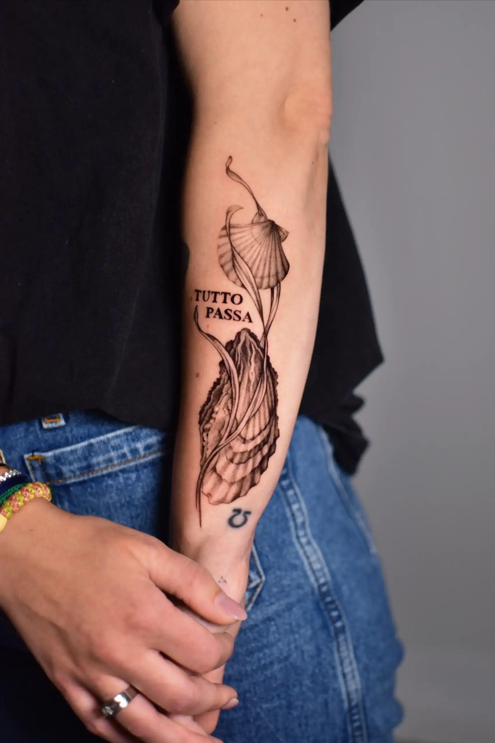 Blackwork tattoo van een oester, schelp en de tekst 'TUTTO PASSA' op de onderarm.