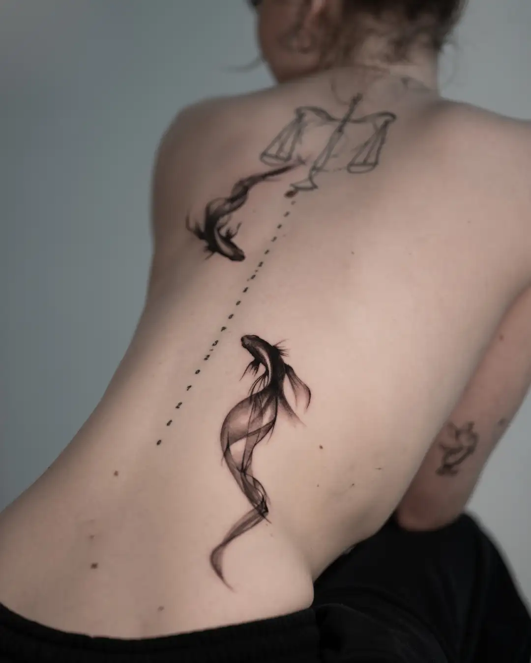 Zwart-wit tattoo van twee vissen en een weegschaal op de rug.