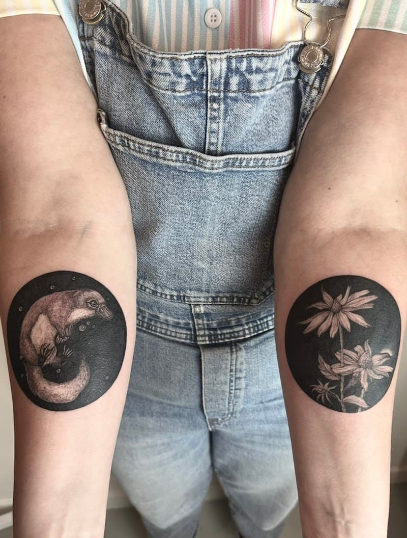 Twee ronde blackwork tattoos: een vogelbekdier en bloemen op de onderarmen.