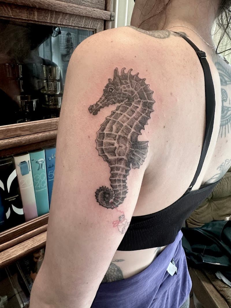 Gedetailleerde zwart-wit zeepaardje tattoo op de bovenarm.