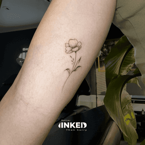 Subtiele fineline bloem tattoo op de achterkant van de bovenarm.