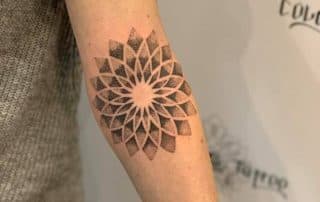 Geometrische dotwork mandala tattoo op onderarm.