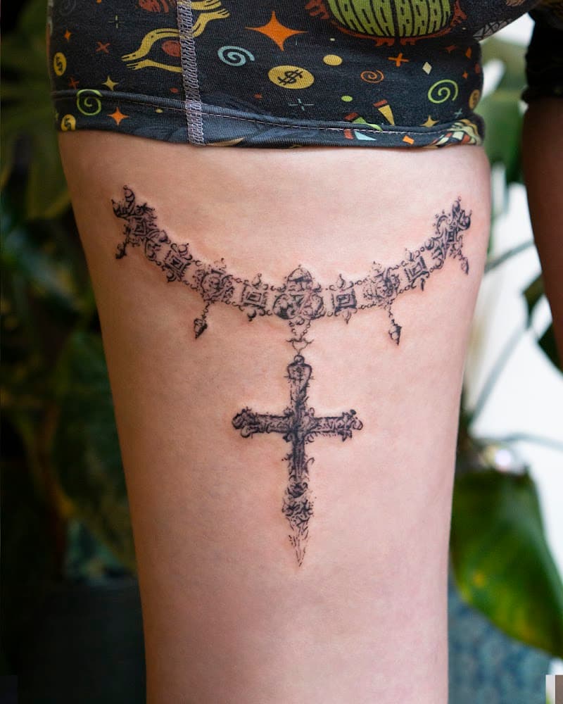 Gedetailleerde ketting met kruis tattoo op bovenbeen.