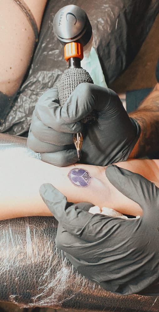 Kleine paarse logo tattoo op de pols tijdens het zetten.