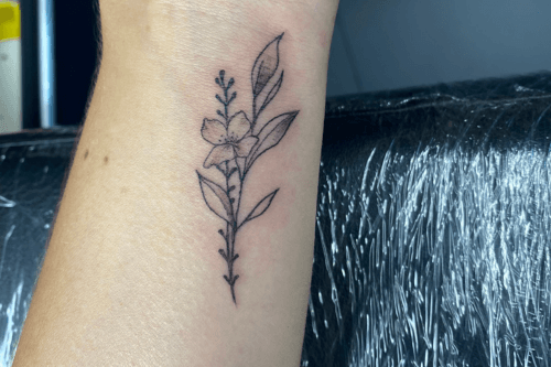 Fineline bloem en bladeren tattoo op de pols.
