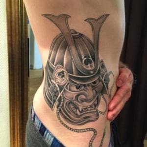 Gedetailleerde zwart-wit samoerai masker tattoo op de zij.