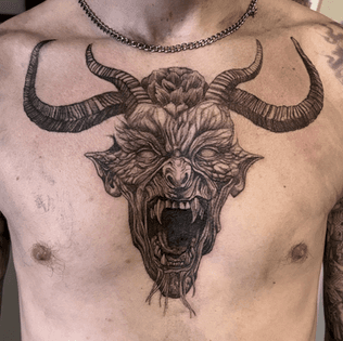 Grote blackwork tattoo van een gehoornde demonenkop op de borst.