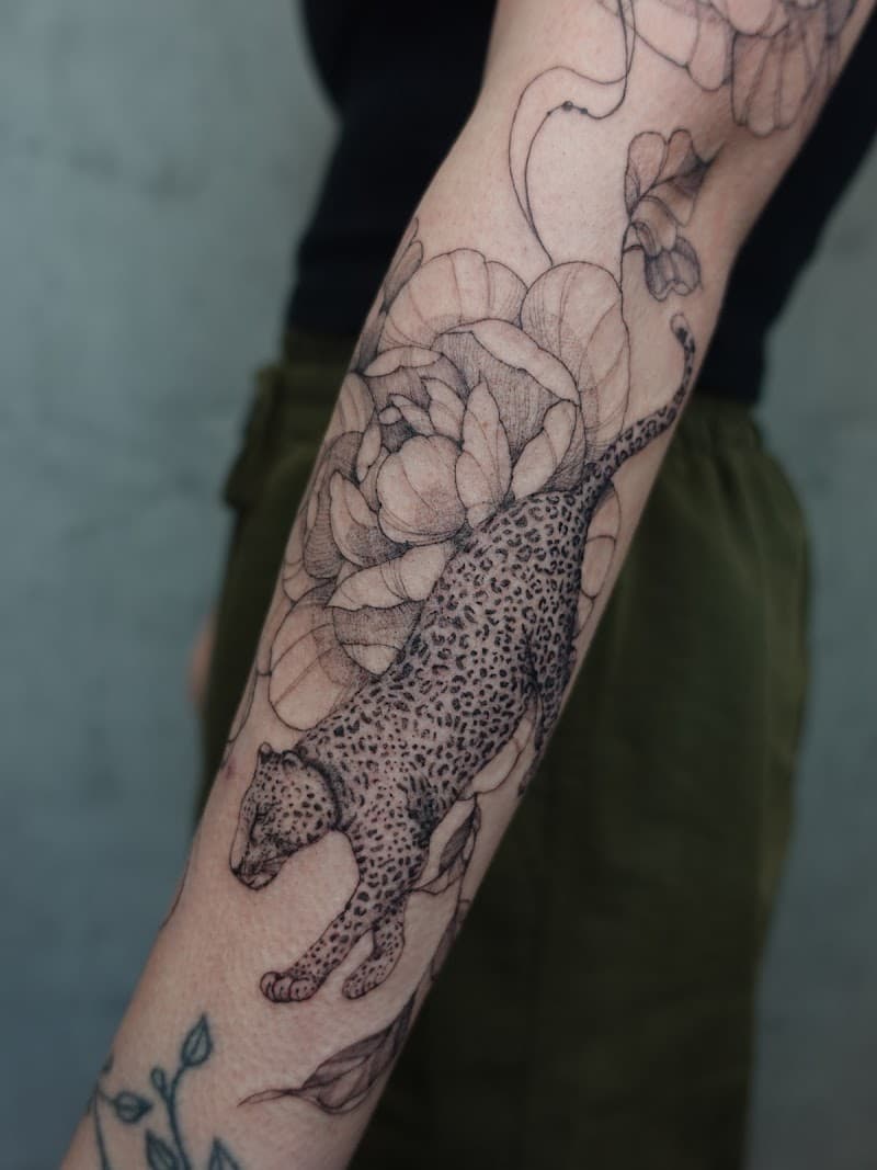 Fineline tattoo van een luipaard en bloemen op de onderarm.