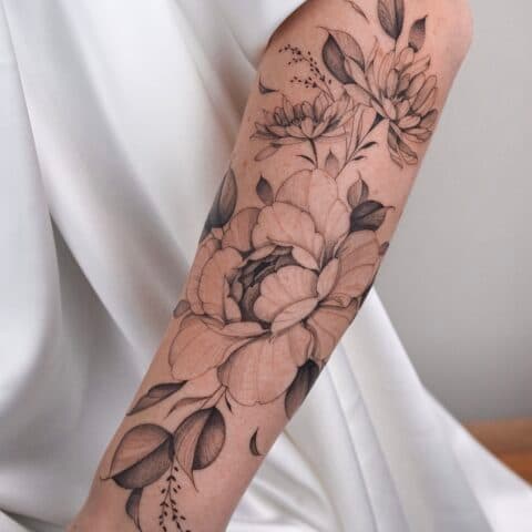 Grote fineline bloemen tattoo op onderarm met dotwork shading.