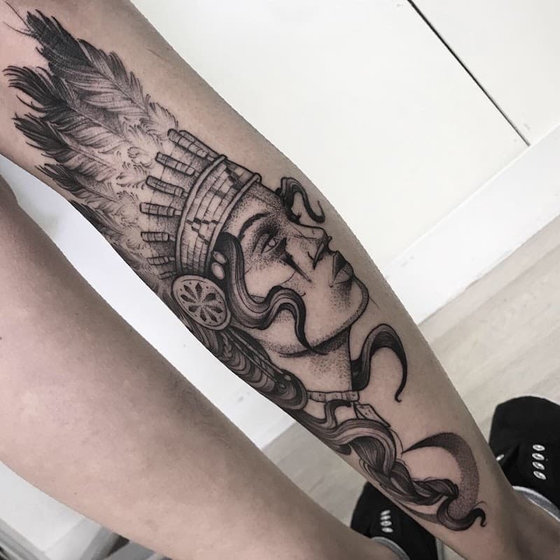 Zwart-wit tattoo van een vrouw met een verentooi op het onderbeen.