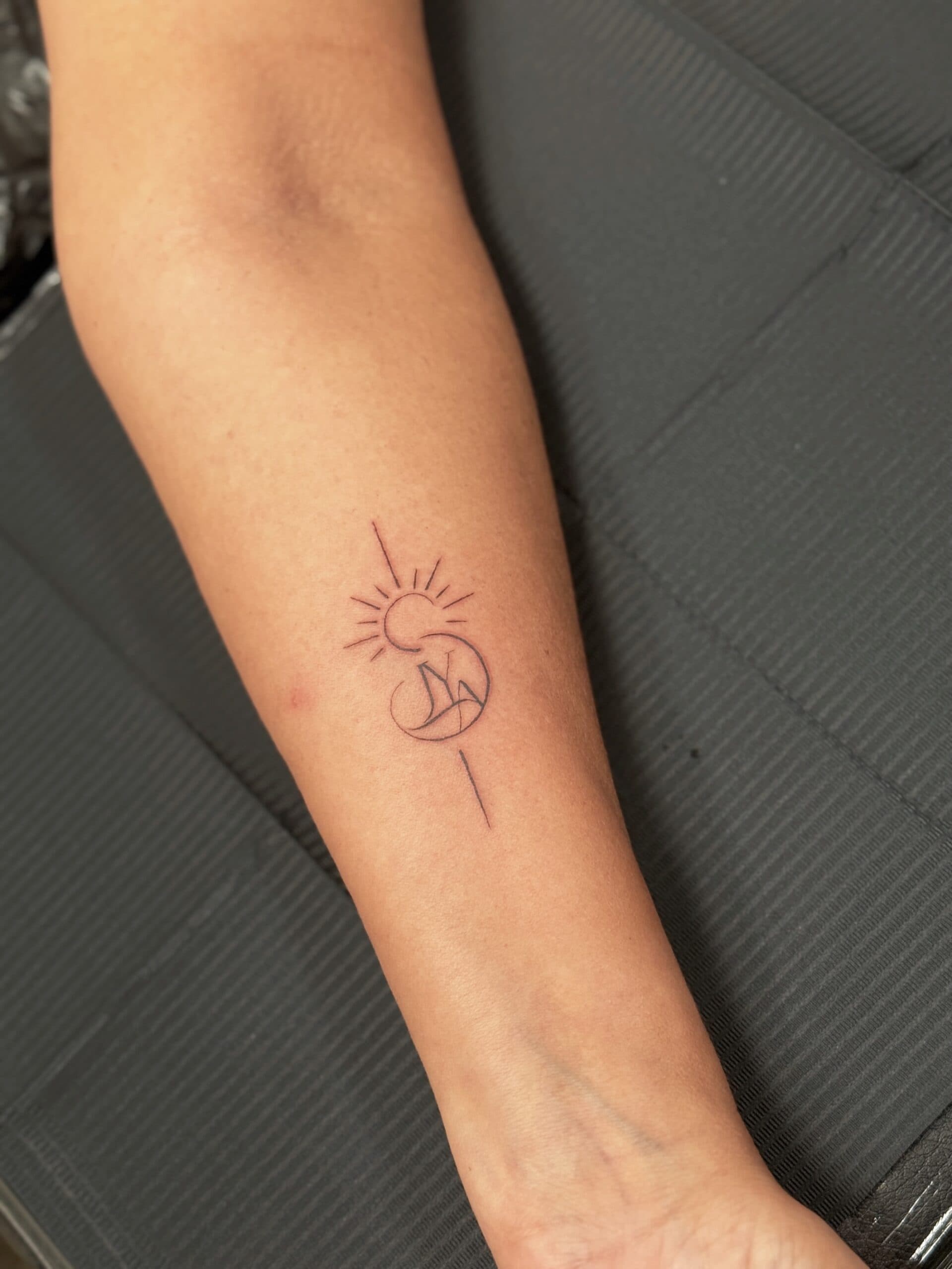 Fineline tattoo van een zon, golf en bergen in een cirkel op de onderarm.