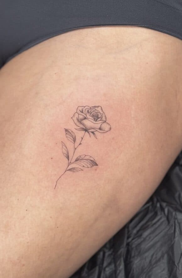 Fijne lijn tattoo van een roos op het bovenbeen.