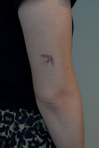 Kleine fineline zwaluw tattoo op de bovenarm.