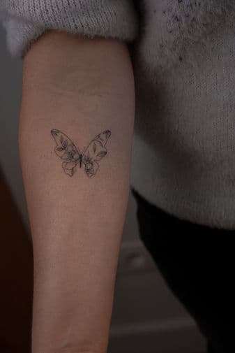 Fineline vlinder met bloemen in vleugels op onderarm.