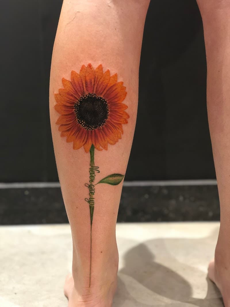 Kleurrijke zonnebloem met 'Never give up' tekst als steel op onderbeen.