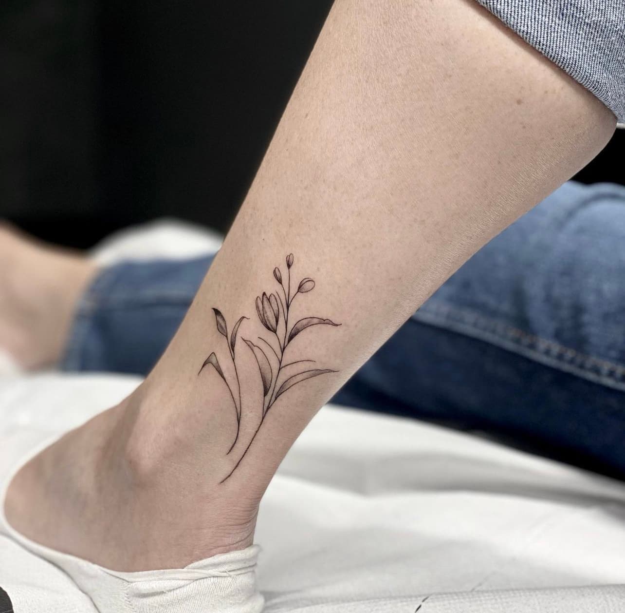 Fineline bloementattoo op de enkel.