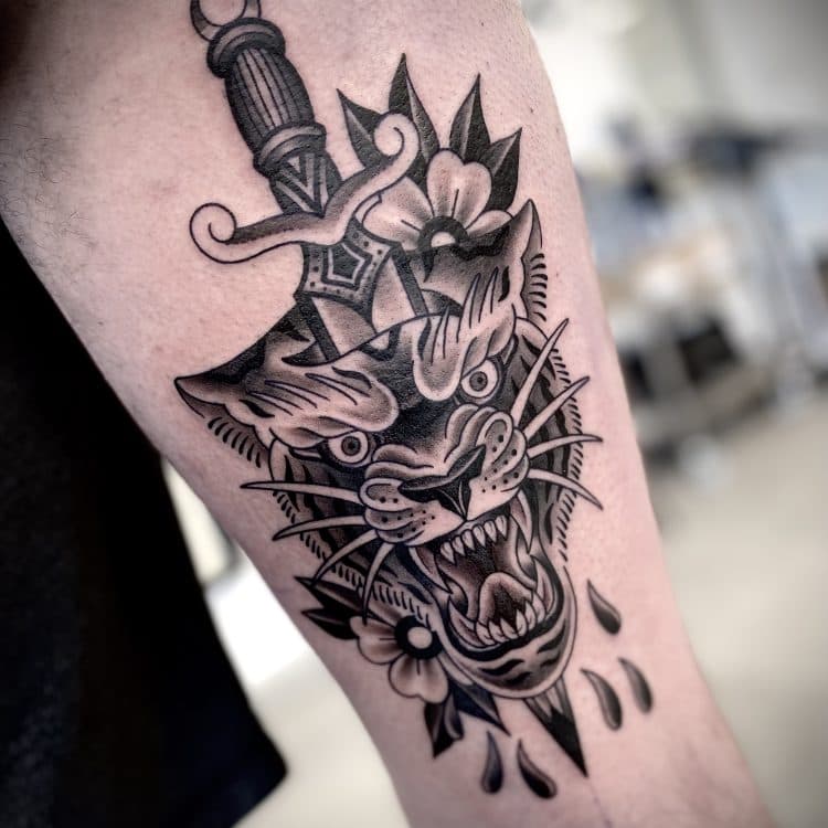 Zwart-wit traditionele tattoo van een dolk door een panterkop met bloemen.