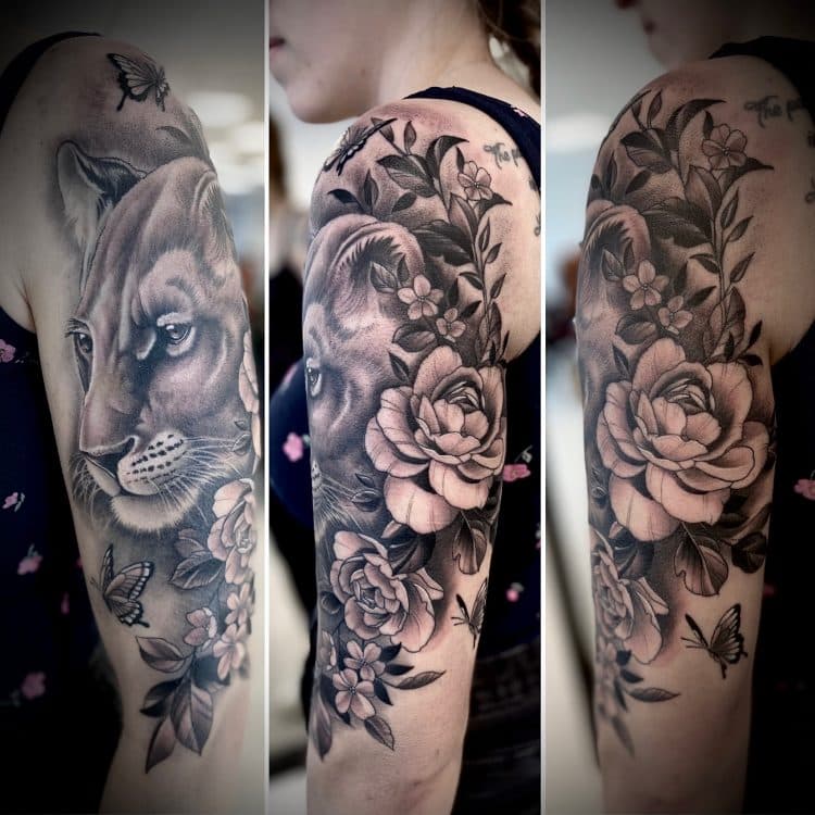 Grote zwart-wit tattoo van een leeuwin met rozen en vlinders op de bovenarm.