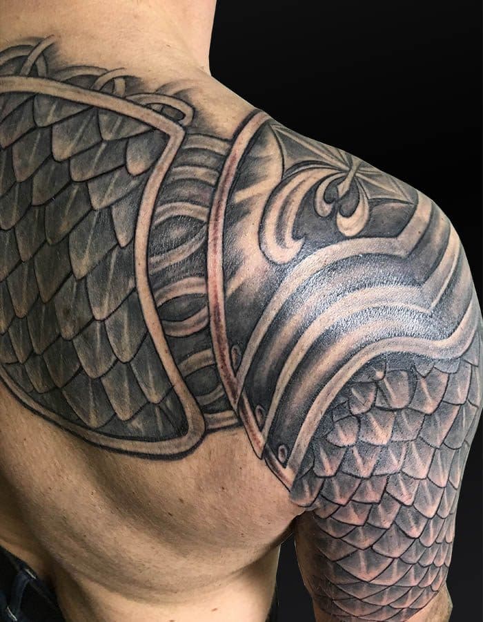 Realistische zwart-wit tattoo van een schubbenharnas op schouder en bovenarm.