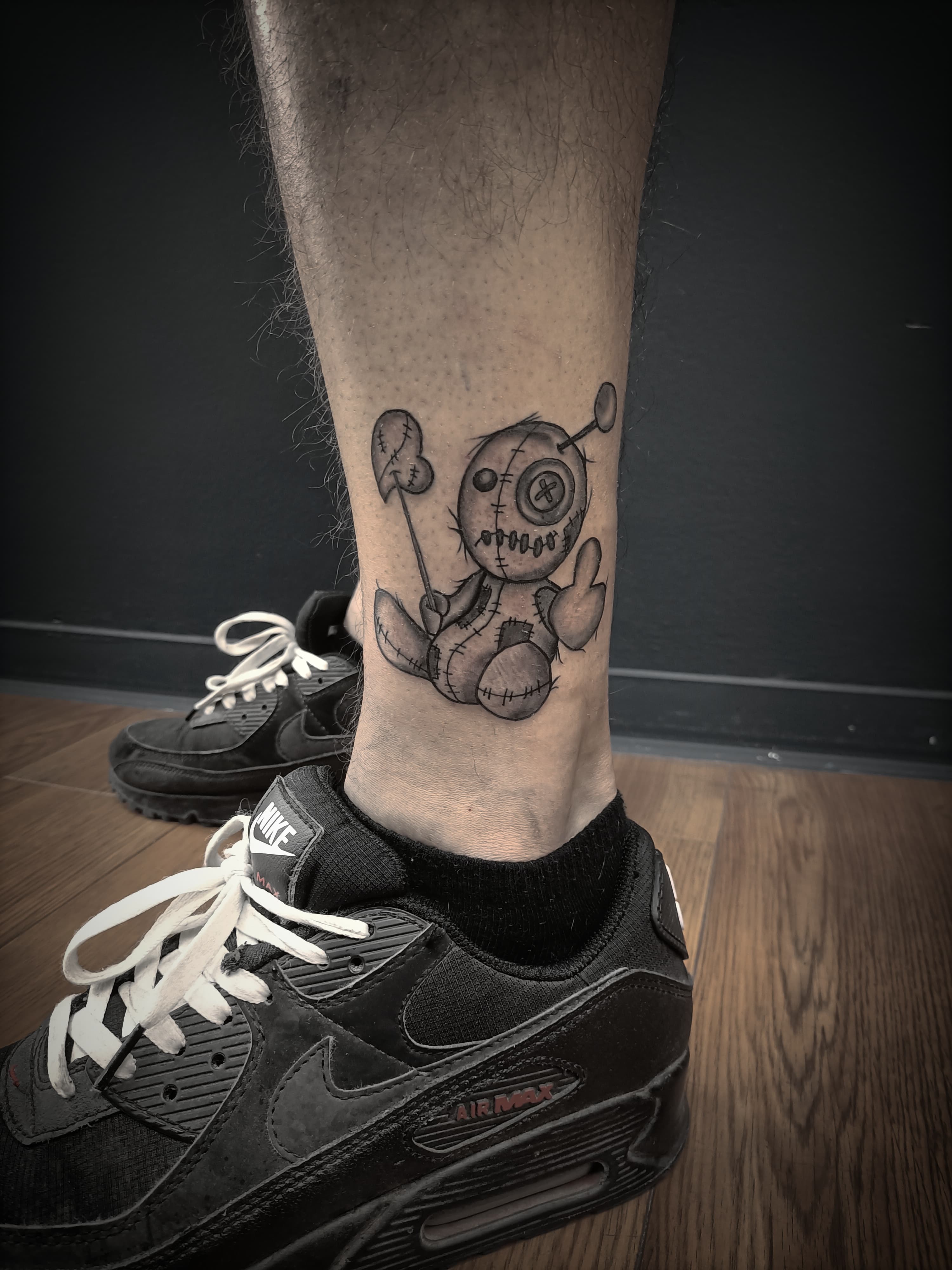 Zwart-wit illustratieve voodoo pop tattoo op de enkel.