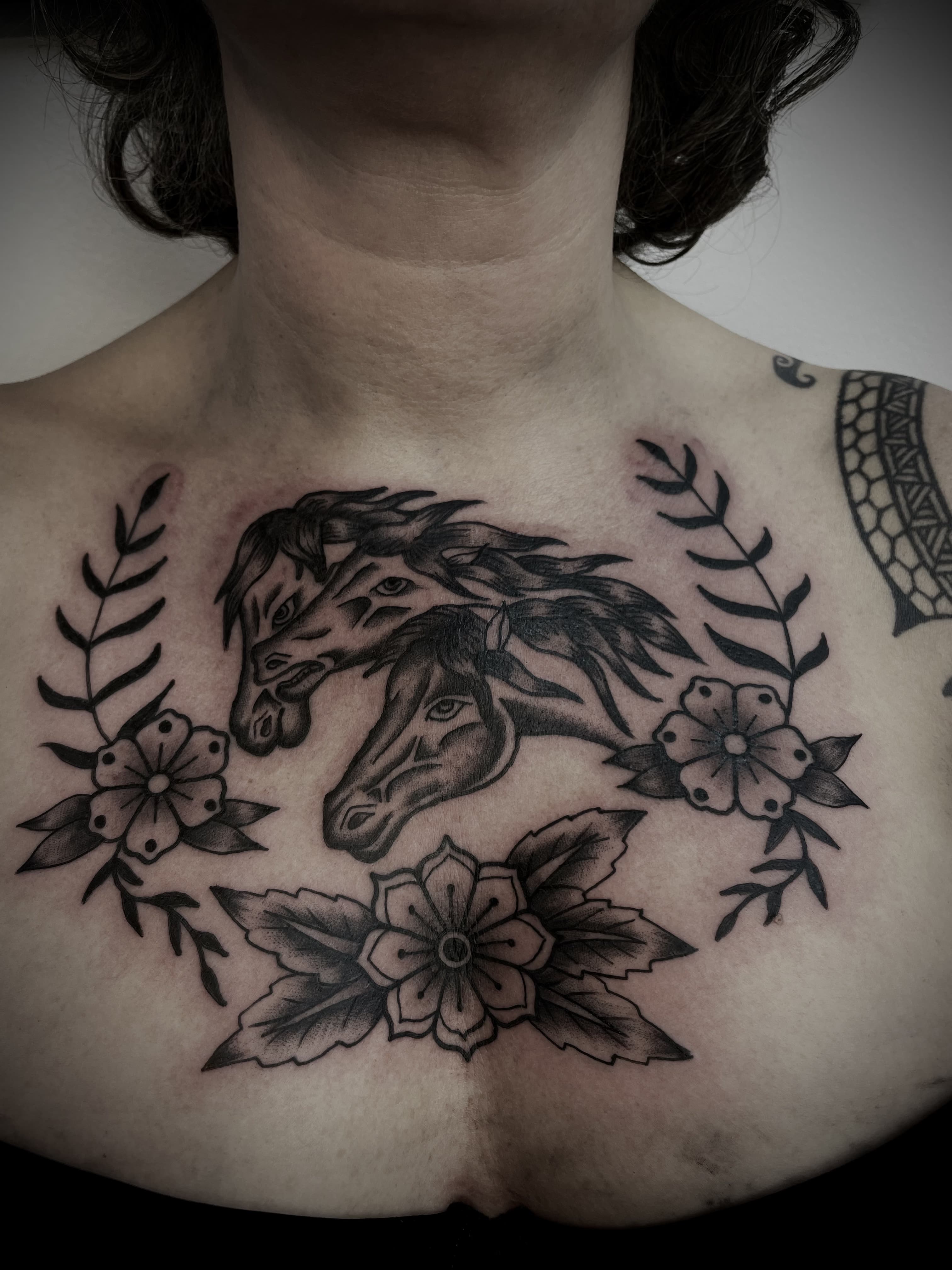 Zwart-wit borststuk met twee paardenhoofden, bloemen en bladeren.