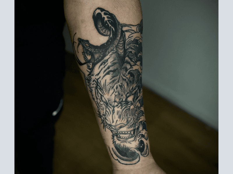 Tijgerkop met slang uit bek en Japanse golven op onderarm.