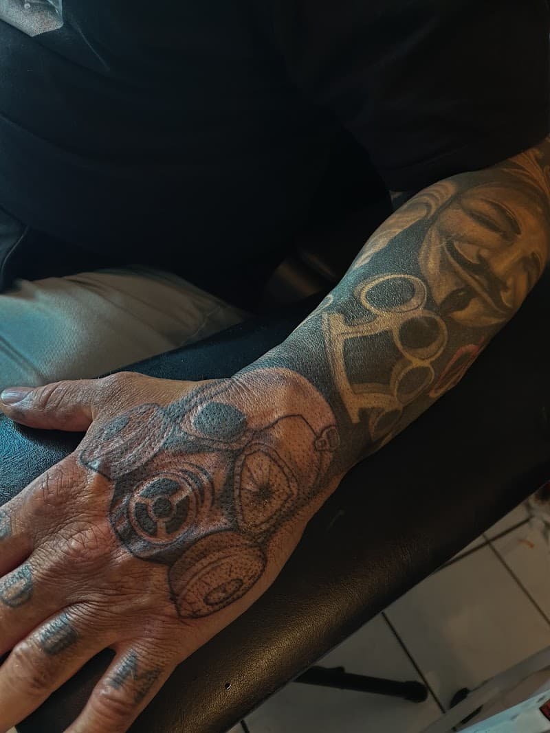 Zwart-wit tattoo van gasmasker op hand en boksbeugel op onderarm.