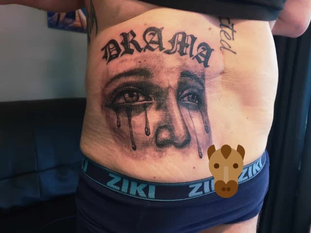 Zwart-wit tattoo op buik van huilende ogen en tekst 'DRAMA'.