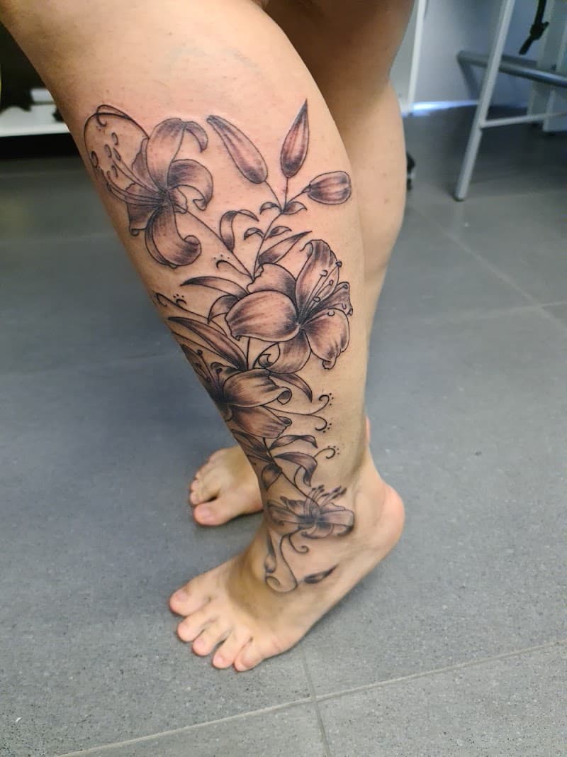 Grote zwart-wit lelie bloemen tattoo op onderbeen en voet.