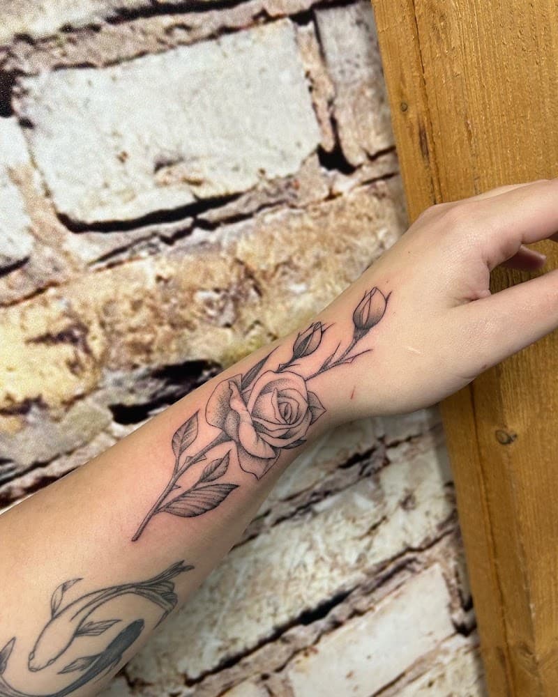 Fineline roos met knoppen en bladeren op de onderarm en pols.