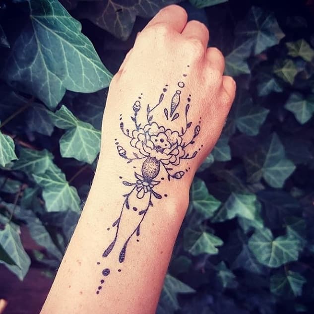 Fineline bloem en ornament tattoo op hand en pols.