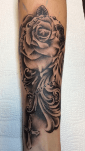 Black & grey tattoo van een roos met een rozenkrans en kruis.