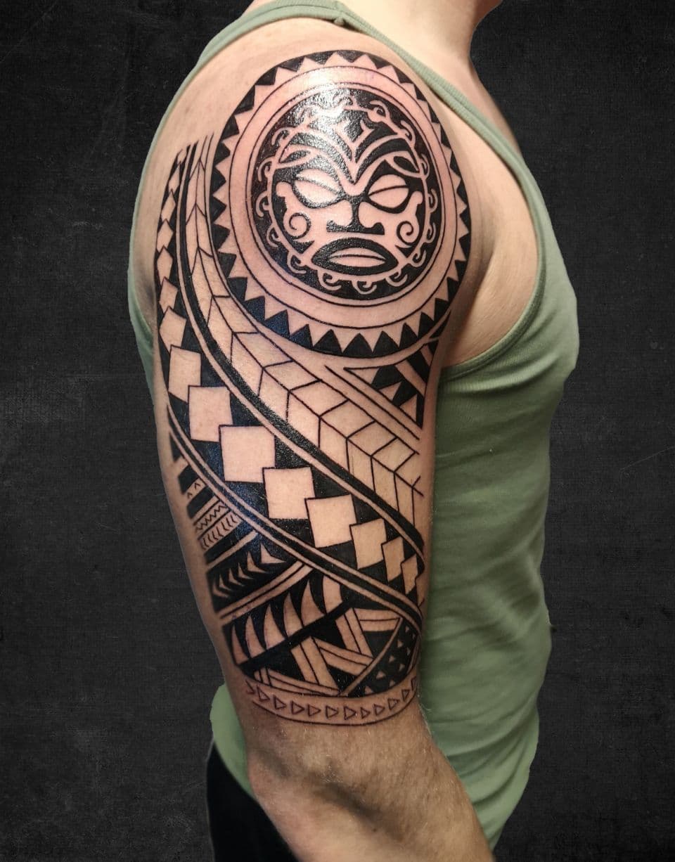 Polynesische tribal tattoo met masker op bovenarm.