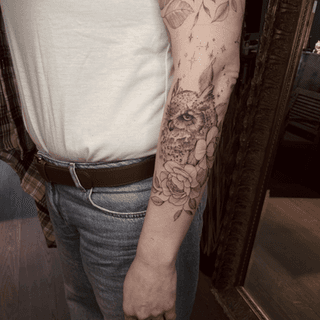 Fineline uil met bloemen en sterren op de onderarm.